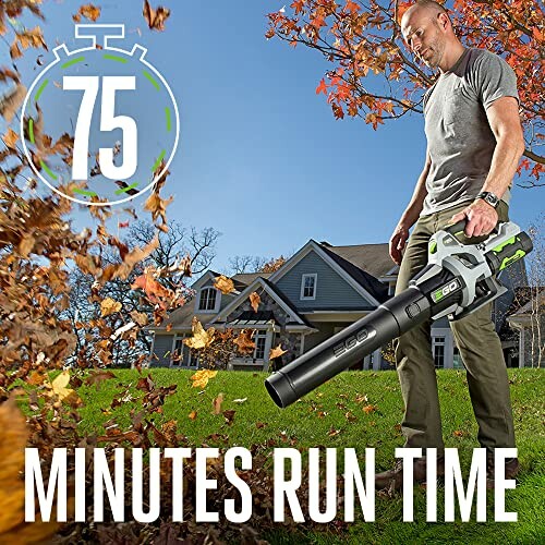 Man using a leaf blower in front of a house with autumn leaves.